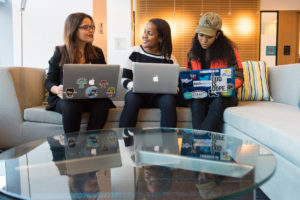 Three women on computers in a discussion.