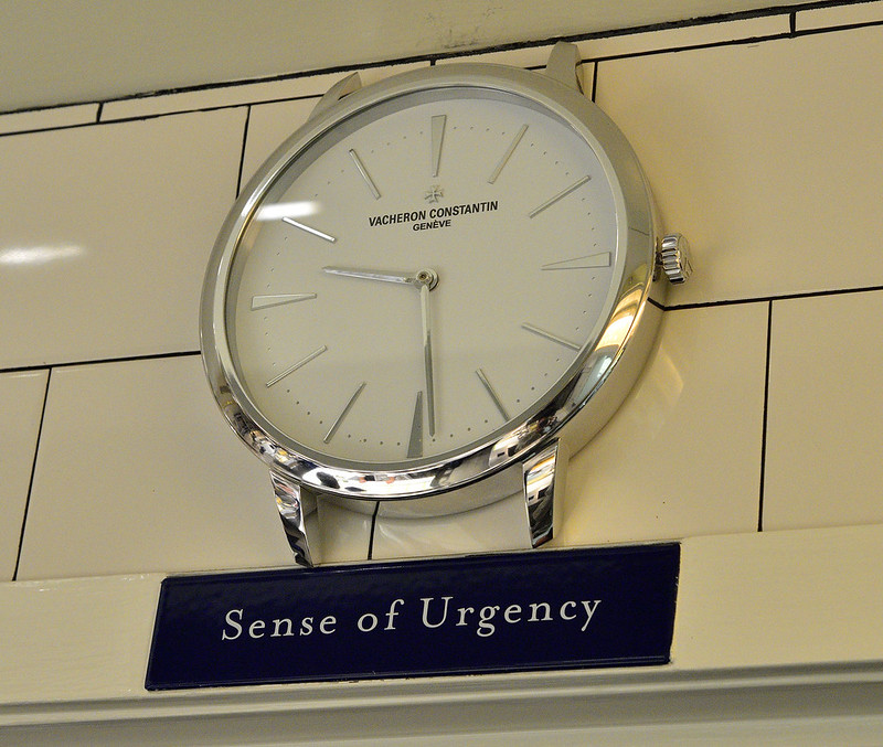 A clock on the kitchen wall of The French Laundry with a black plaque reading "Sense of Urgency" beneath it